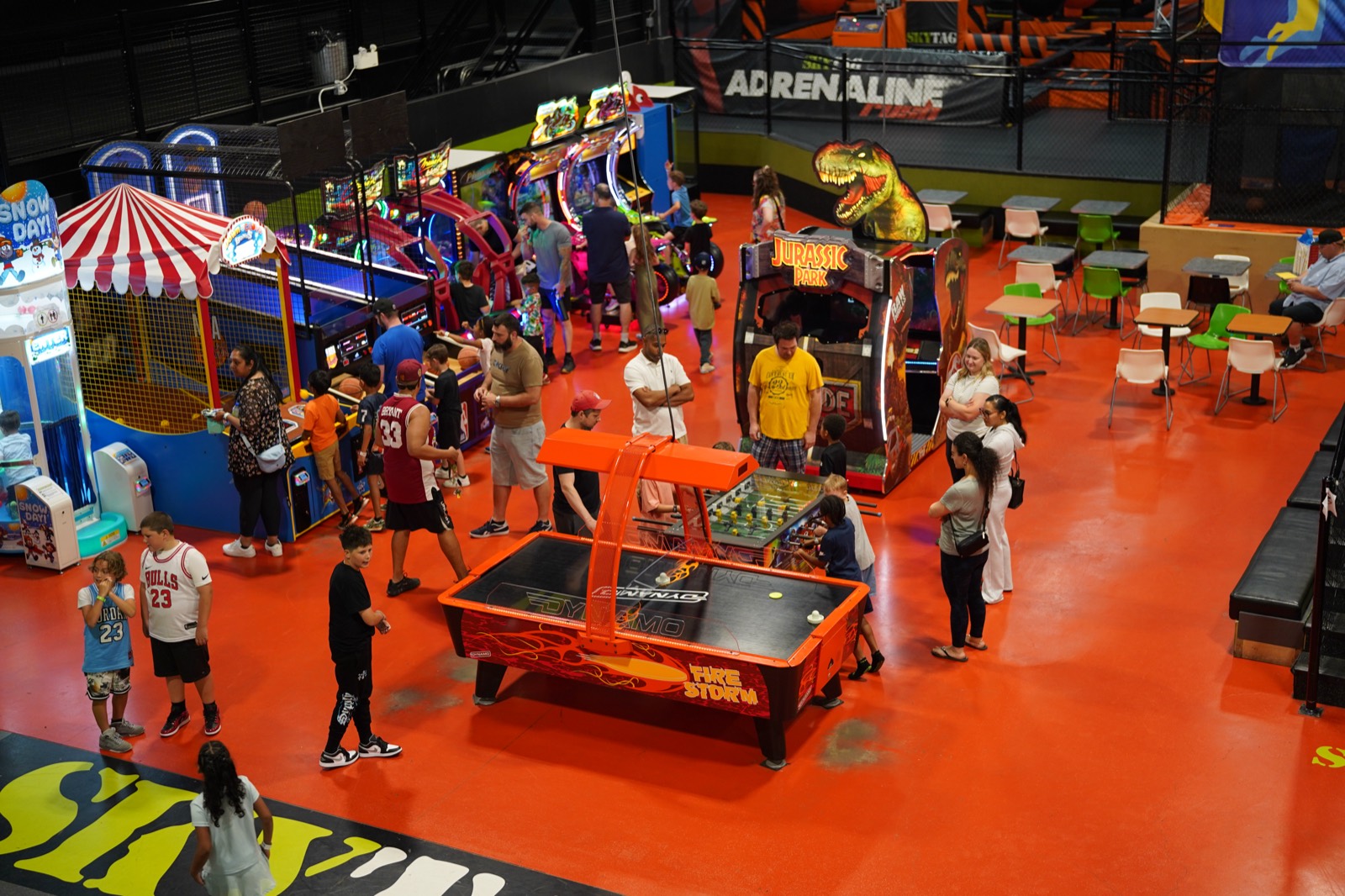 Families playing air hockey, foosball and arcade cabinets across the orange arcade floor at SkyTag Dollard-Des-Ormeaux