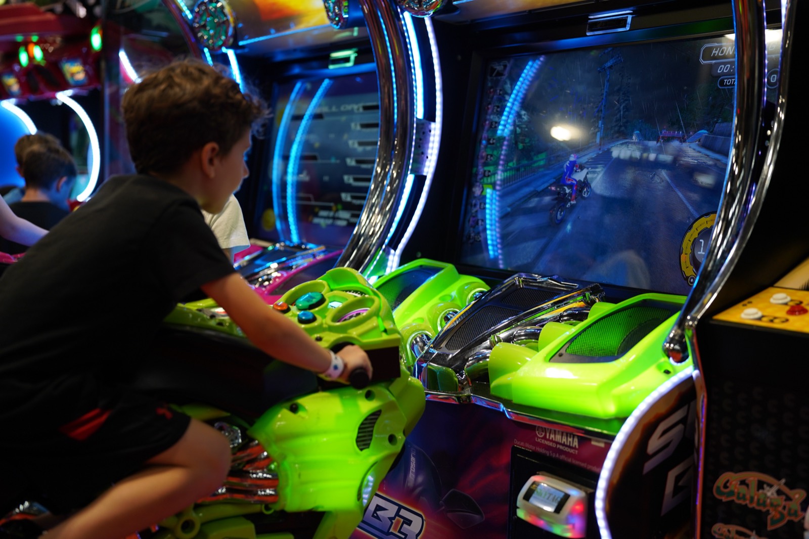 Child riding a neon-lit motorbike racing cabinet at the SkyTag arcade in Montreal